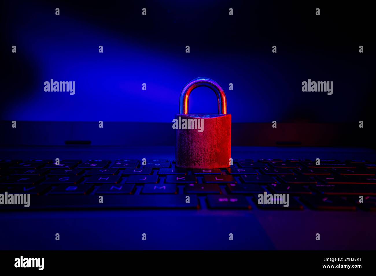 Un lucchetto chiuso poggia su una tastiera nera del notebook, illuminata da una luce blu e rossa. Foto Stock