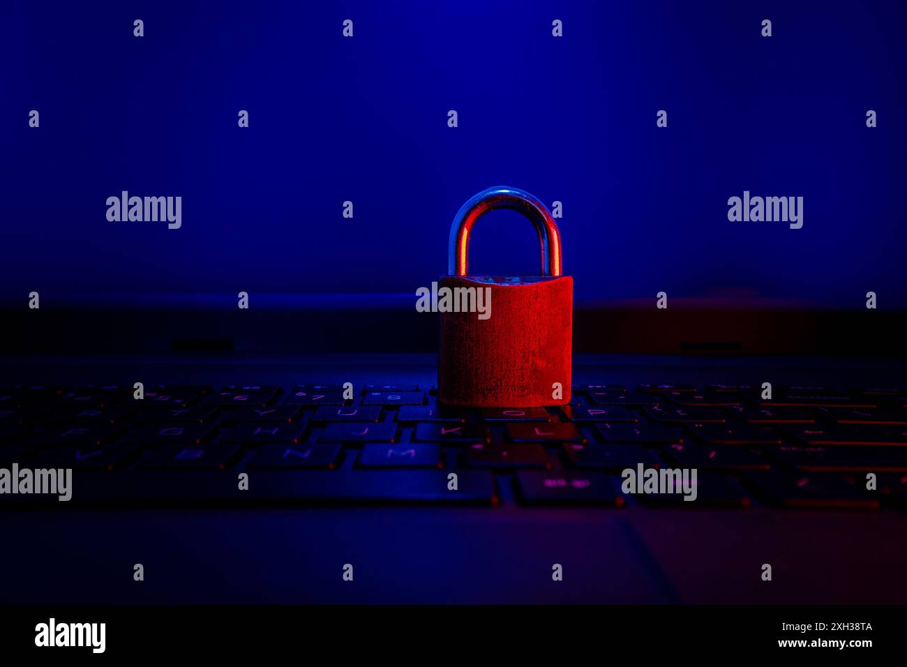 Un lucchetto rosso si trova sulla tastiera di un computer, illuminato da luci blu e rosse. Foto Stock