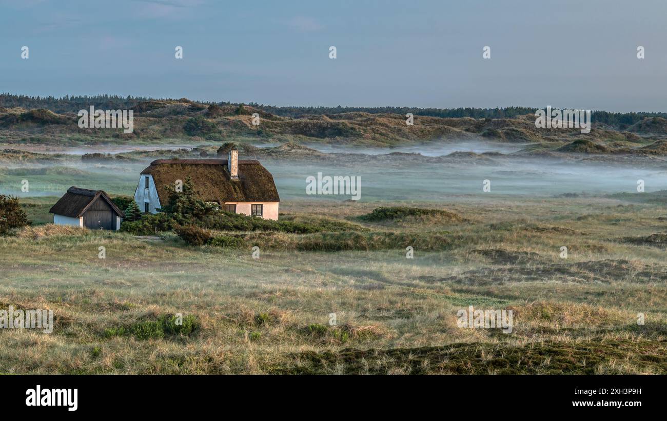 Vecchia casa solitaria di paglia tra le dune quando la nebbia si stabilizza alla luce della sera, Skagen, Danimarca, 30 maggio 2024 Foto Stock