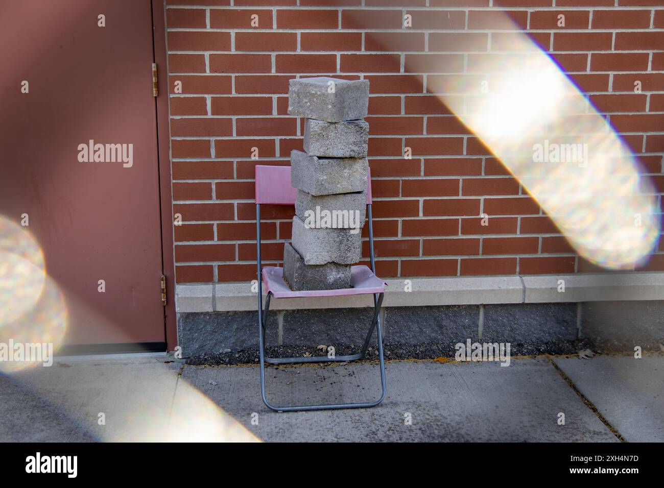 Scena urbana illuminata dal sole - blocchi di cemento impilati su una sedia rosa contro una parete di mattoni rossi - effetto flare della lente. Presa a Toronto, Canada. Foto Stock