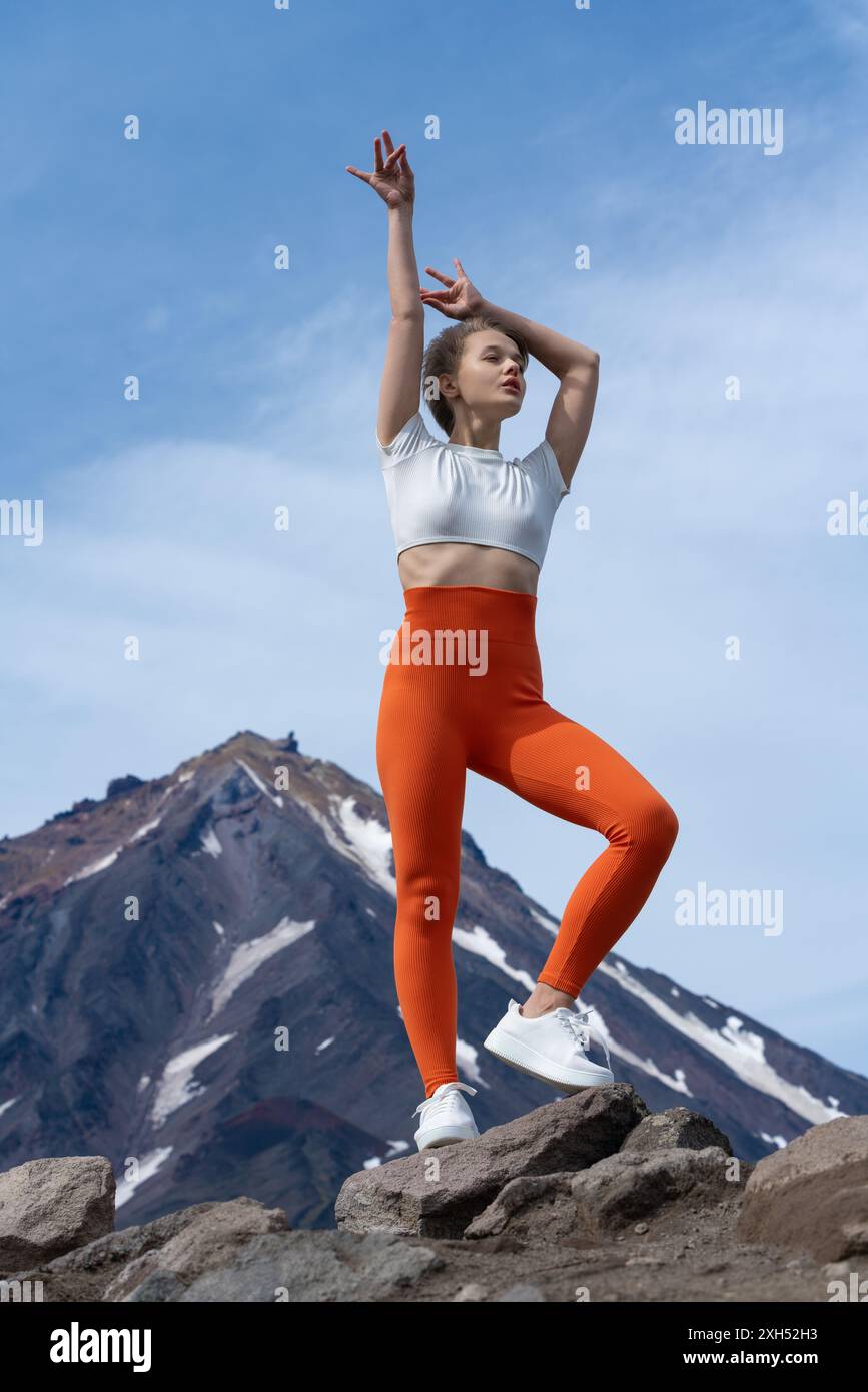 Felice e serena atleta si erge in montagna sullo sfondo del cono vulcanico. Bellissimo istruttore di yoga biondo e sottile con capelli corti è dres Foto Stock