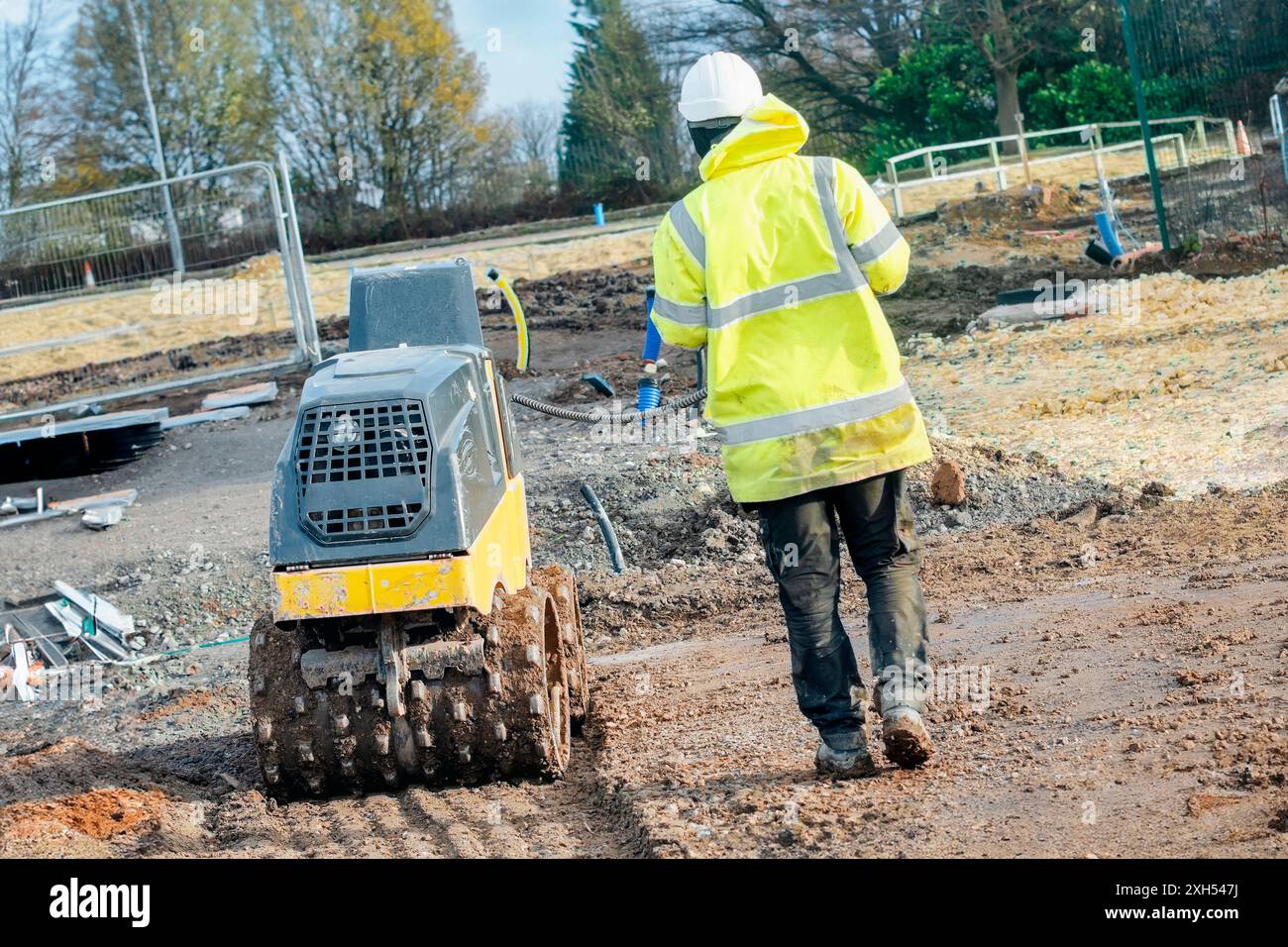 Rullo trincea con controllo remoto azionato da un lavoratore a terra per compattare il terreno nel nuovo cantiere di sviluppo di abitazioni. Stia lontano dalla pianta in movimento Foto Stock