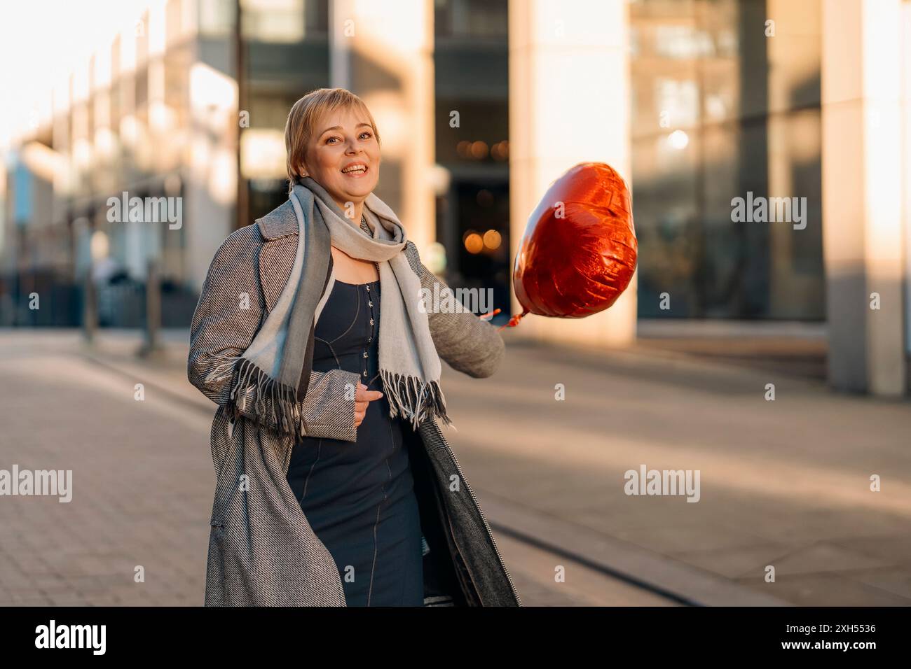 Donna felice di mezza età con una mongolfiera a forma di cuore che si innamora, che trascorre una giornata di divertimento, passeggiando per la città inglese la primavera è in the Air Lifestyle, tour Foto Stock