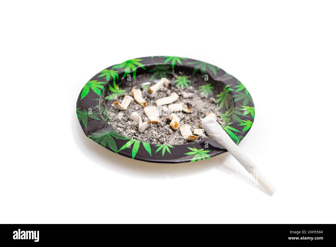 Sigaretta articolare di marijuana su un portacenere sporco con motivi a foglie di cannabis, piatta isolata su bianco Foto Stock
