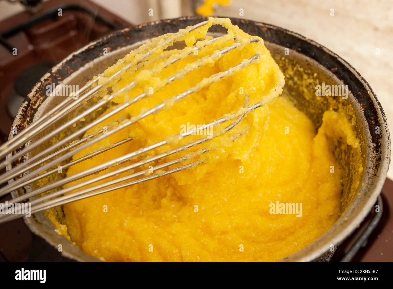 Bollire la farina di mais in una pentola di ghisa, preparare mamaliga, cibo tradizionale rumeno e mescolare Foto Stock