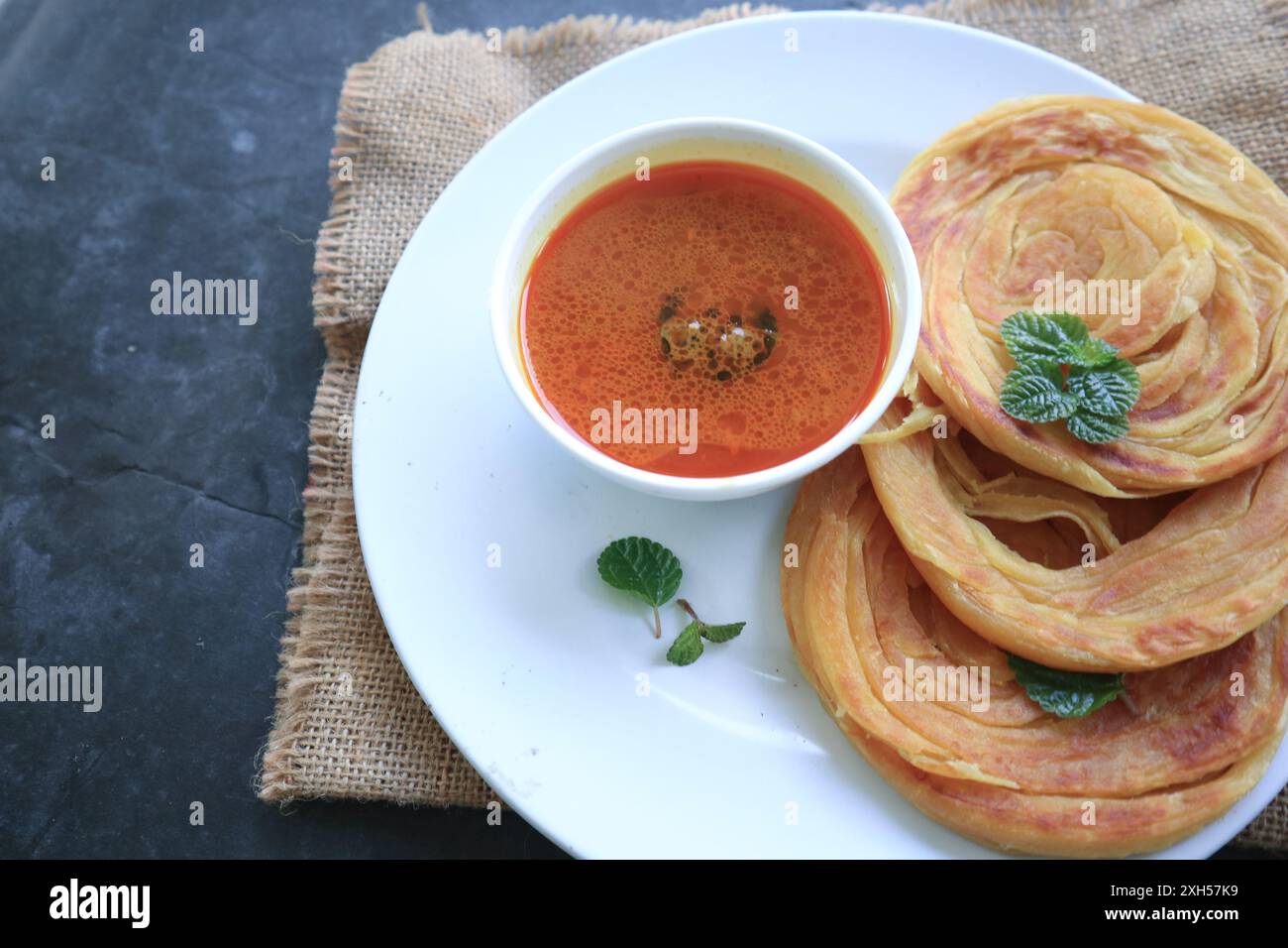 Pane Roti Canai o Paratha con salsa al curry, scaglie di peperoncino e yogurt, su pancetta Foto Stock