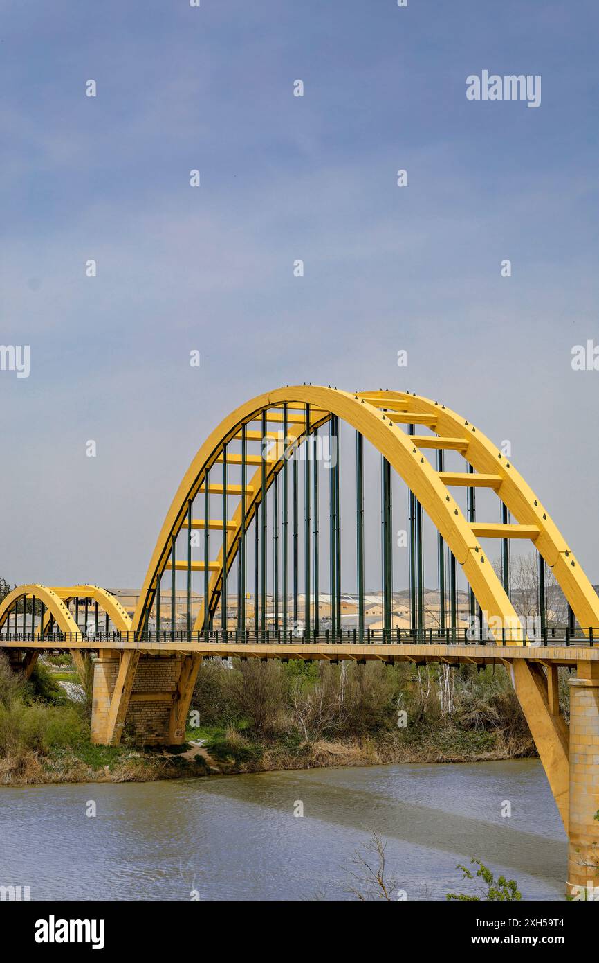 Un ponte giallo attraversa un fiume, con un cielo blu chiaro sullo sfondo. Il ponte è un grande arco, e l'acqua sottostante è calma. Concetto di tranqui Foto Stock