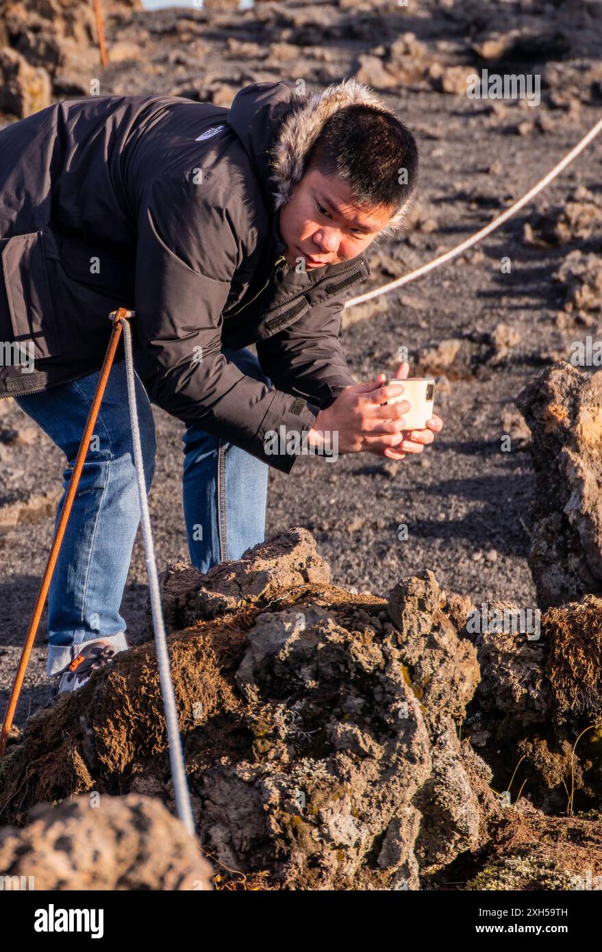 l'uomo asiatico sta fotografando i dettagli di una roccia vulcanica con il suo smartphone. L'uomo indossa una giacca nera e un jeans Foto Stock