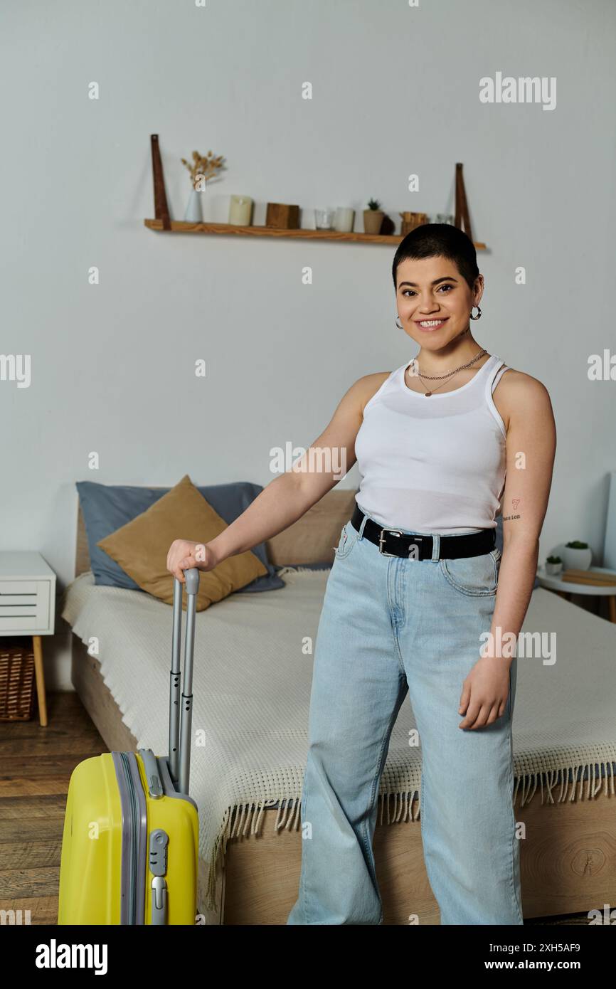 Giovane donna con capelli corti in piedi accanto a una valigia gialla, che fa le valigie per una vacanza e un viaggio. Foto Stock