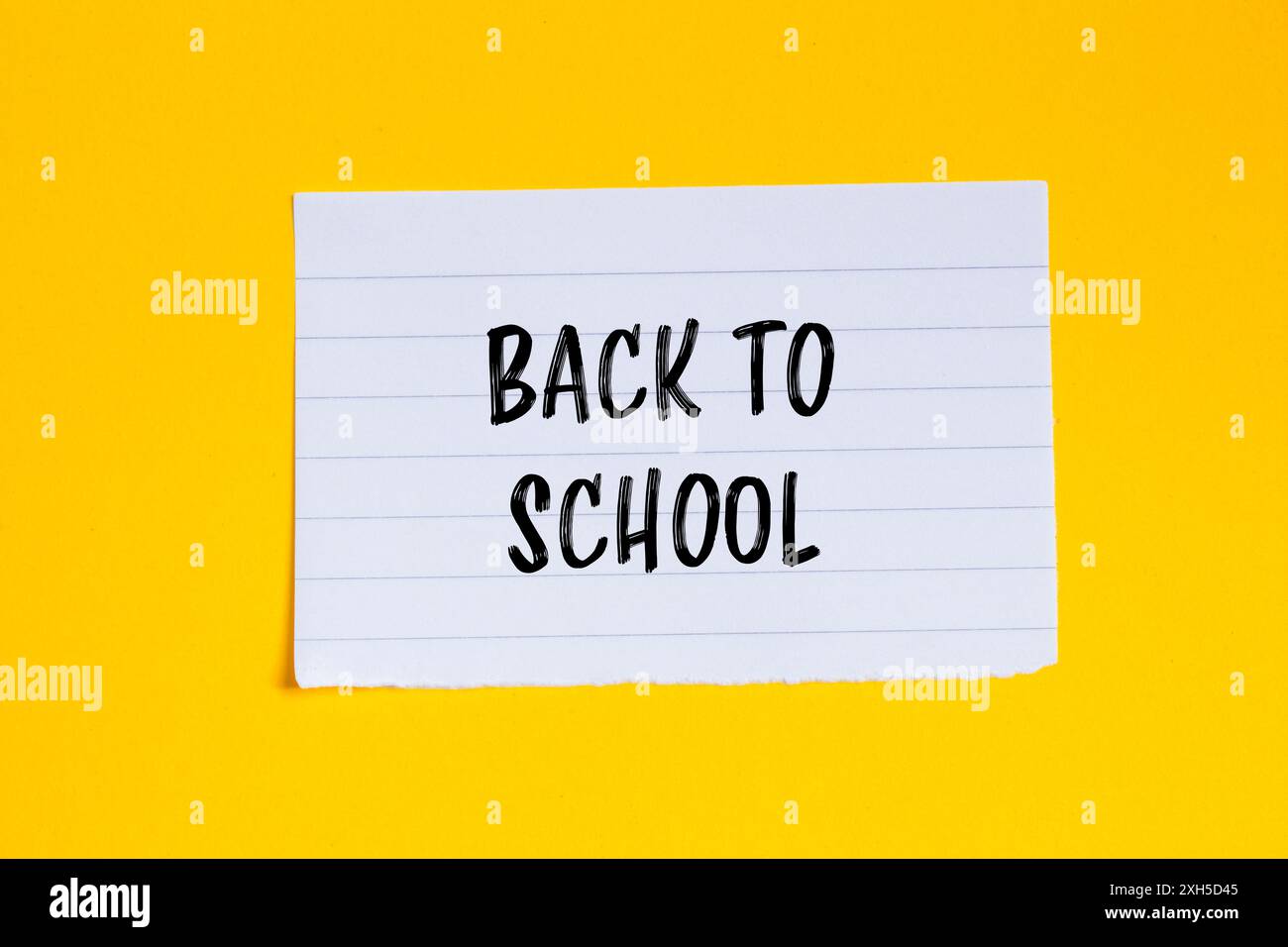 Messaggio di ritorno a scuola scritto su un pezzo di carta bianca strappato con sfondo giallo. Simbolo concettuale di ritorno a scuola. Copia spazio. Foto Stock