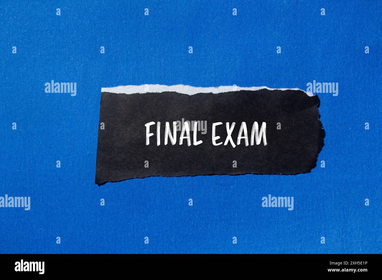 Messaggio finale dell'esame scritto su un pezzo di carta nera strappato con sfondo blu. Simbolo dell'esame finale concettuale. Copia spazio. Foto Stock
