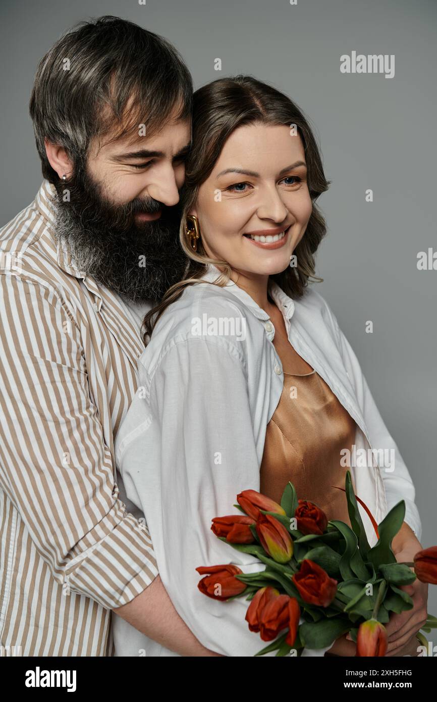 Una coppia con un abbigliamento elegante, l'uomo che tiene la donna vicino mentre sorride e regge un bouquet di tulipani. Foto Stock