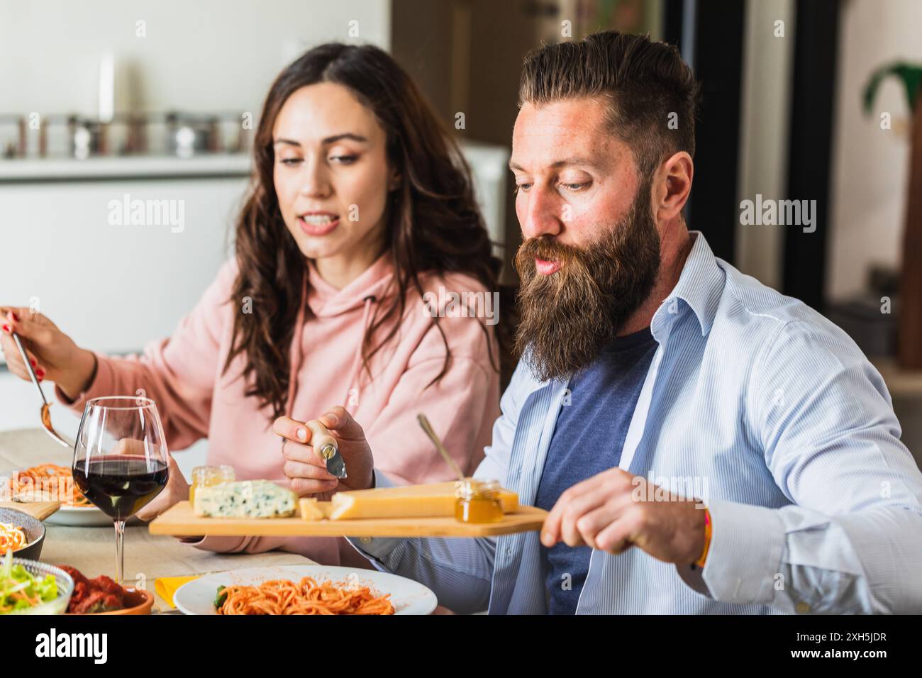 Coppia felice che si gusta un tagliere di formaggi e vino con la loro cena di pasta a casa Foto Stock