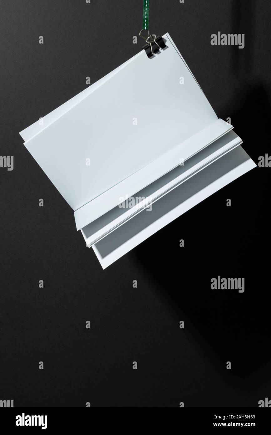 I fogli di carta bianca vuoti sono appesi da una graffetta su uno sfondo nero, con spazio per la copia. Ideale per i grafici, l'immagine presenta uno spazio pulito Foto Stock