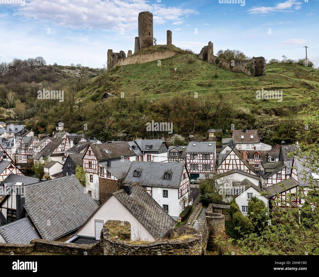Affascinanti case in legno lungo un fiume con un castello medievale su una collina nebbiosa a Monreal, Germania. Foto Stock