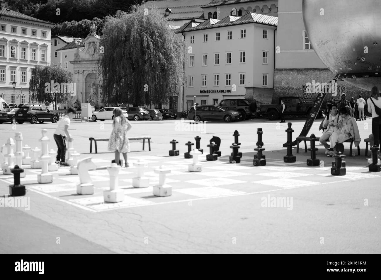 Bambini che giocano con una scacchiera gigante ambientata in una piazza urbana con edifici storici Foto Stock