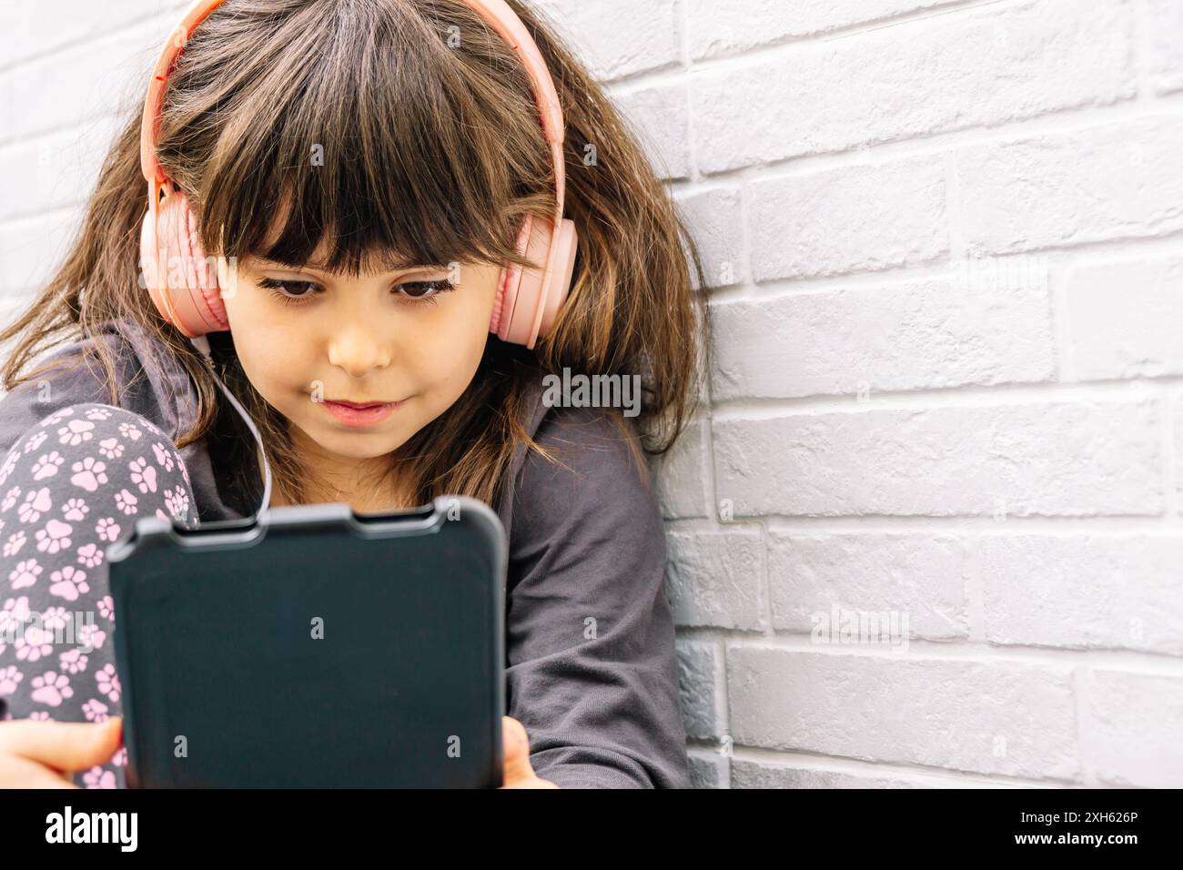 La bambina spagnola guarda lo schermo del tablet mentre indossa le cuffie. Concetto di uso tecnologico nei bambini. Orizzontale con spazio di copia. Foto Stock