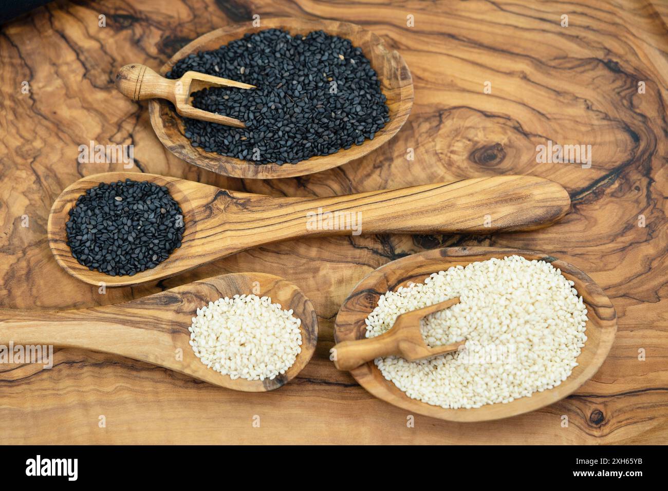 sesamum, sesamo (Sesamum indicum), semi di sesamo sbucciati e non sbucciati in piccole ciotole di legno con cucchiai di legno e cucchiai di legno Foto Stock