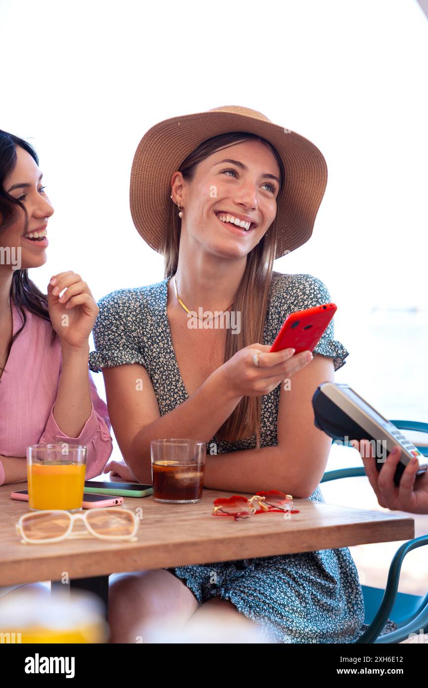 Le giovani donne pagano con un pagamento contactless tramite l'app per telefoni cellulari nel ristorante Foto Stock