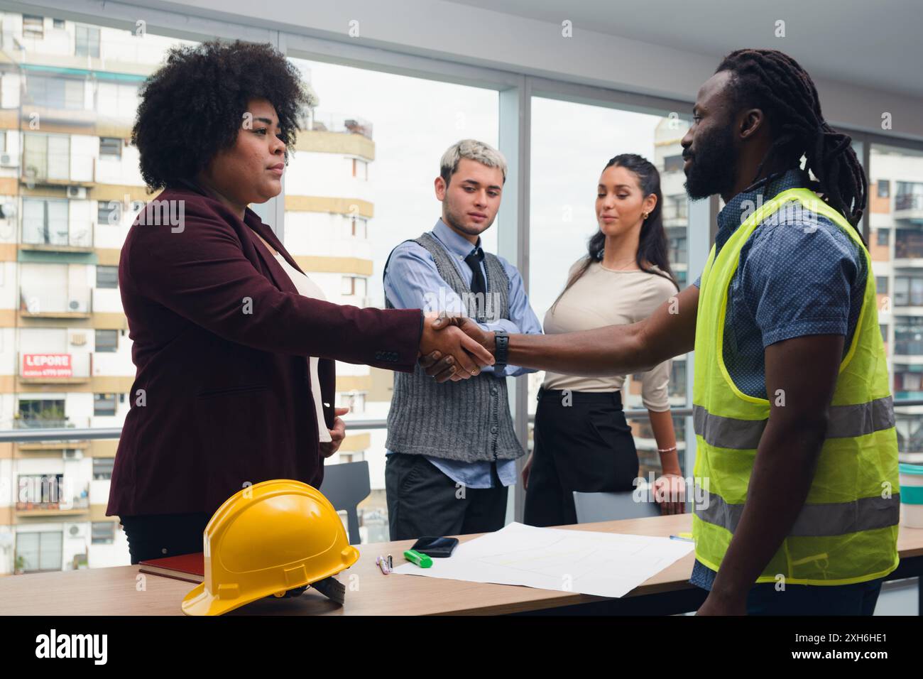 Uomo ingegnere e donna appaltante che stringono la mano dopo la riunione per chiudere il contratto, sono all'interno dell'ufficio intorno al tavolo con i documenti sopra, ci sono Foto Stock