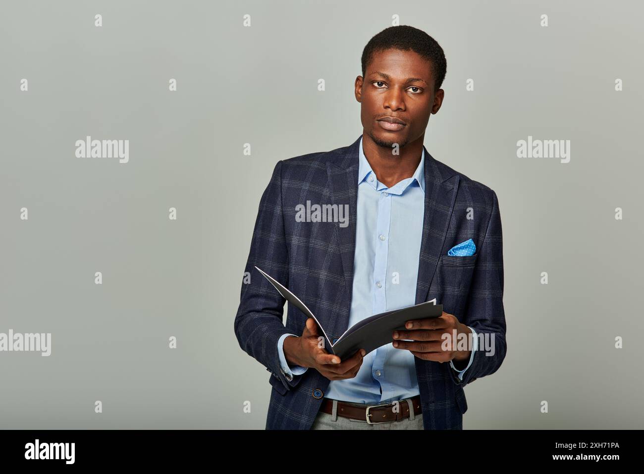 L'uomo afroamericano in un blazer a scacchi ha una cartella, trasudando professionalità in un ambiente commerciale formale. Foto Stock