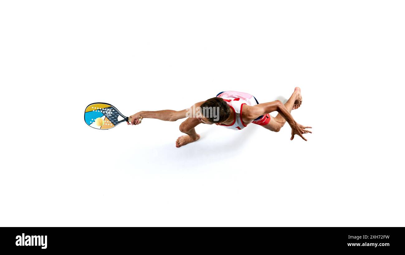 Tiro aereo di atleta maschile, giocatore di Beach tennis con canotta e pantaloncini corti, palla con pagaia multicolore isolata su sfondo bianco Foto Stock