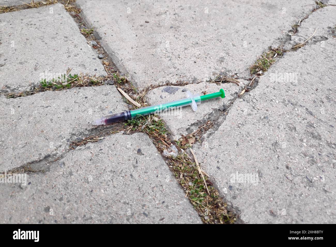 Primo piano su una siringa usata lasciata sul marciapiede da un tossicodipendente. Foto Stock