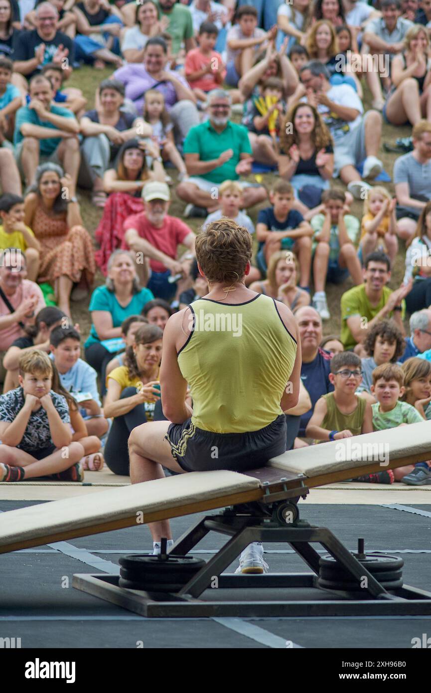 Viladecasn, SPAGNA - 11 LUGLIO 2024: Un artista si siede con il dorso rivolto verso una folla attenta in un evento all'aperto, mettendo in evidenza l'interazione del pubblico a. Foto Stock