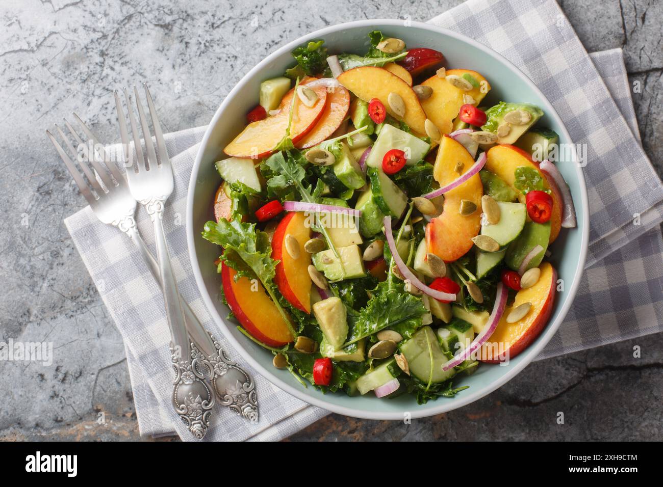 Insalata piccante con nettarina, avocado, cetrioli, cipolla rossa, peperoncino, rucola, spinaci e semi di zucca da vicino in un recipiente sul tavolo. Orizzontale superiore vi Foto Stock