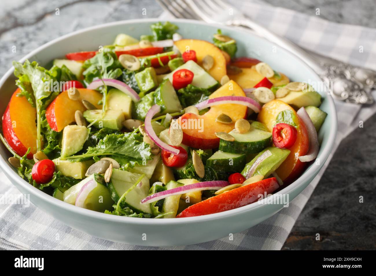 Insalata estiva fresca con pesca, avocado, cetrioli, cipolla rossa, peperoncino, rucola, spinaci e semi di zucca da vicino in un recipiente sul tavolo. Orizzontale Foto Stock