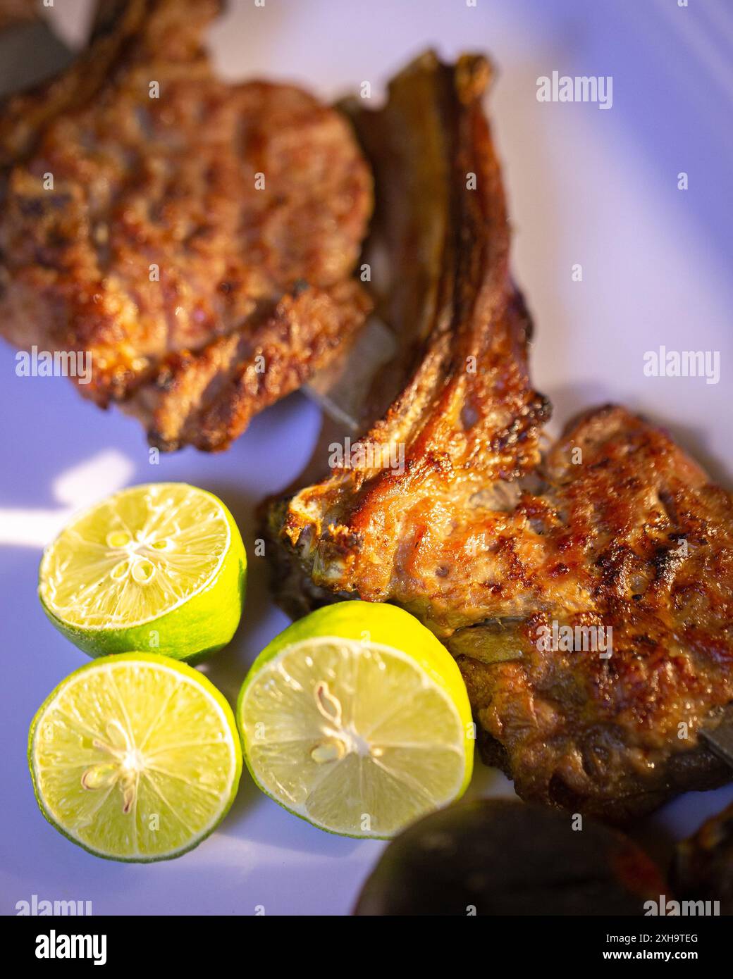 Deliziosa carne alla griglia servita con metà di lime fresche su un piatto bianco, pronta per essere gustata. Foto Stock