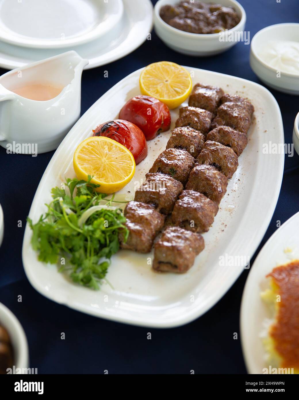 Piatto di kebab persiani servito con pomodori grigliati, erbe fresche e limone, un classico piatto mediorientale. Foto Stock