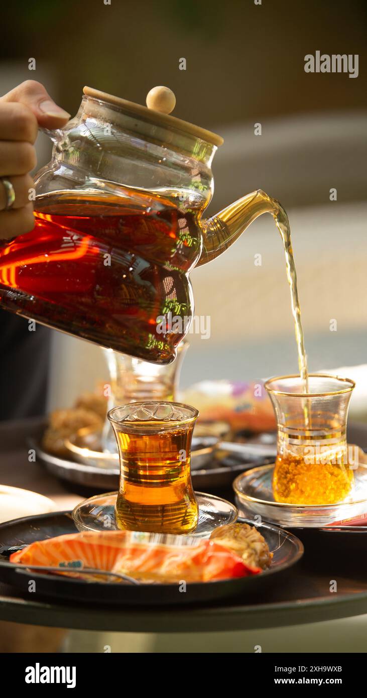 Versare il tradizionale tè persiano, servito con deliziosi dolci, perfetto per un pomeriggio rilassante Foto Stock