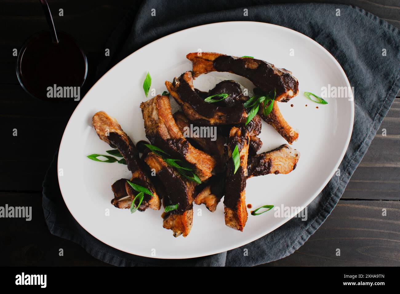 Costolette di maiale con salsa Black Garlic-Miso su un piatto da portata: Piatto di costolette di schiena condite con salsa barbecue salata guarnite con scalpelli Foto Stock
