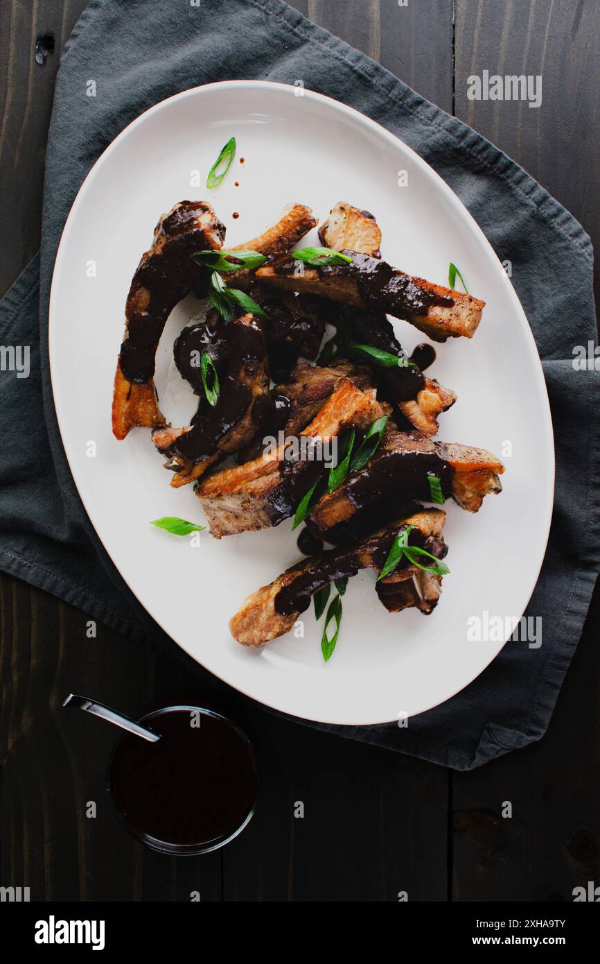 Costolette di maiale con salsa Black Garlic-Miso su un piatto da portata: Piatto di costolette di schiena condite con salsa barbecue salata guarnite con scalpelli Foto Stock