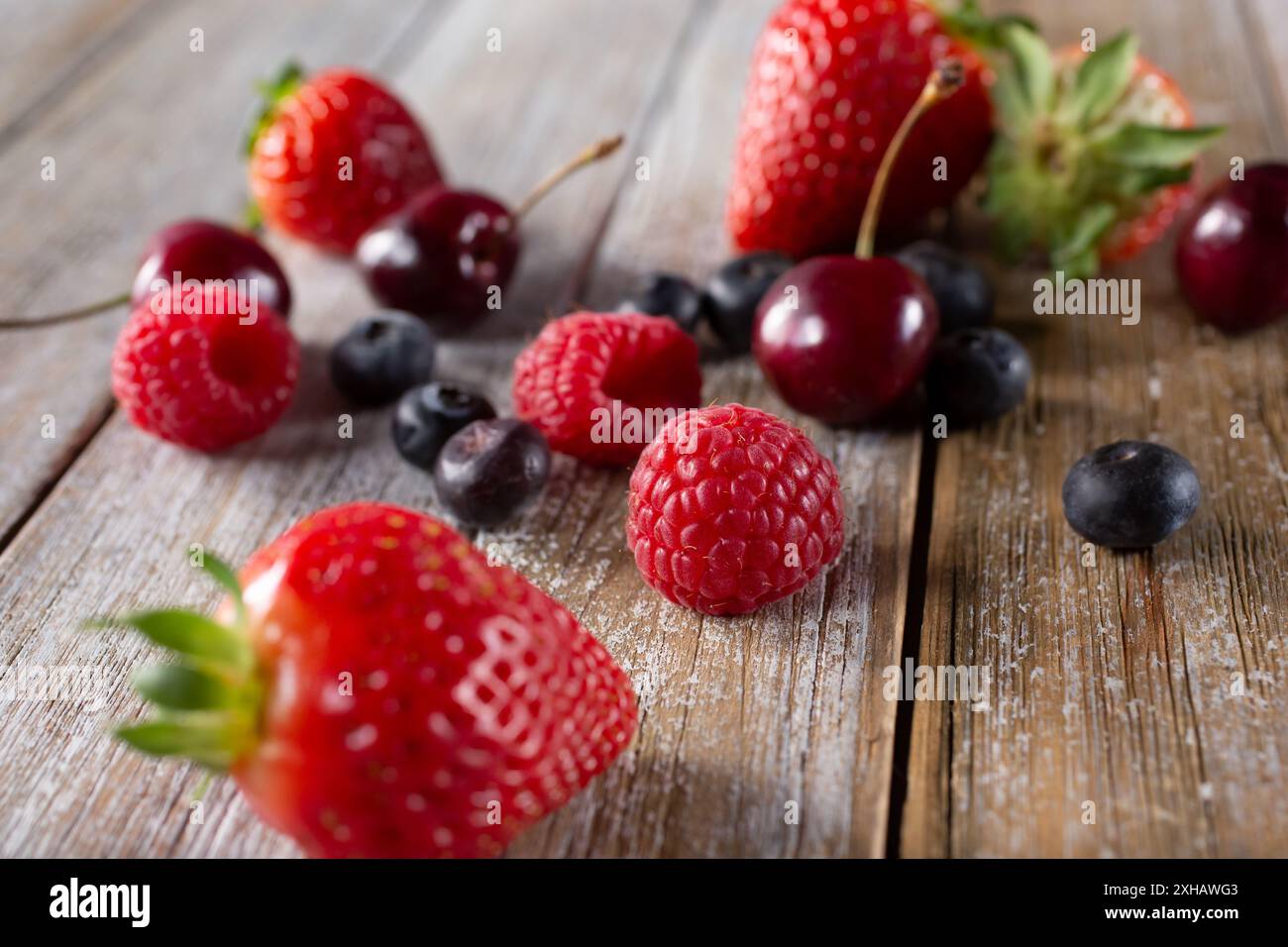 Vista di una varietà di frutta sparsi su una superficie di legno, caratterizzata da fragole, mirtilli, lamponi e ciliegie. Foto Stock