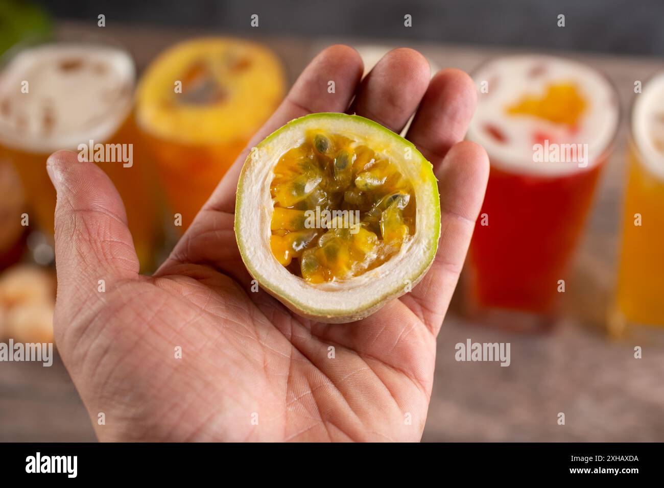 Una vista di una mano che tiene mezzo frutto della passione con diverse bevande a base di tè alla frutta. Foto Stock