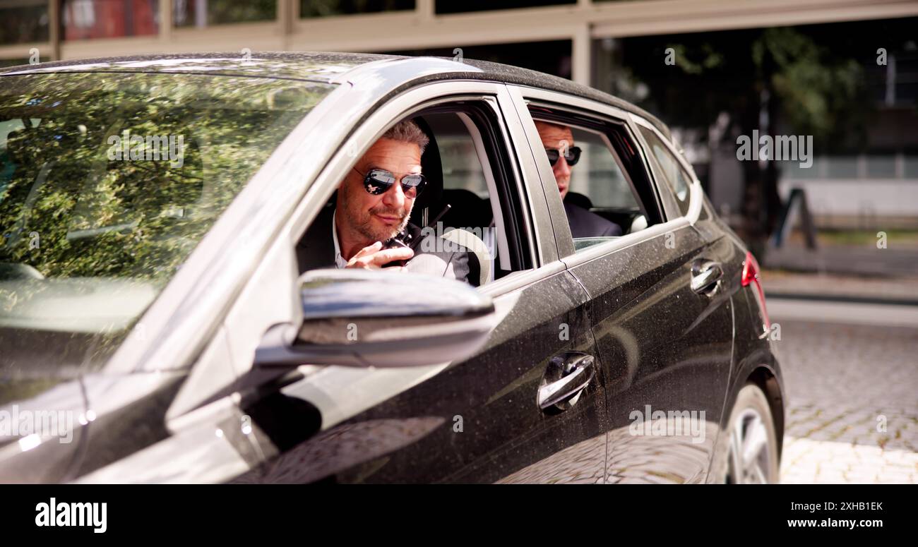 Investigatore riservato in occhiali da sole che fa affari all'interno di un'auto di lusso con un cliente di alto profilo. Guardia di sicurezza personale, detective, consulente d'affari Foto Stock