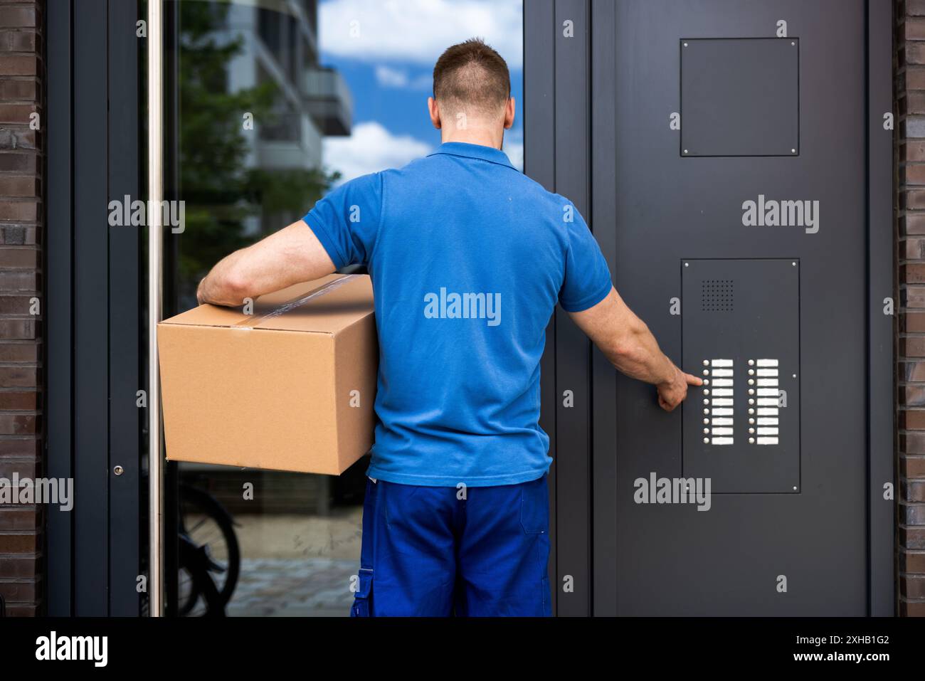Corriere professionale che garantisce consegne sicure dei pacchi con sistema interfono avanzato all'ingresso dell'edificio, identità verificata per ogni ordine. Foto Stock
