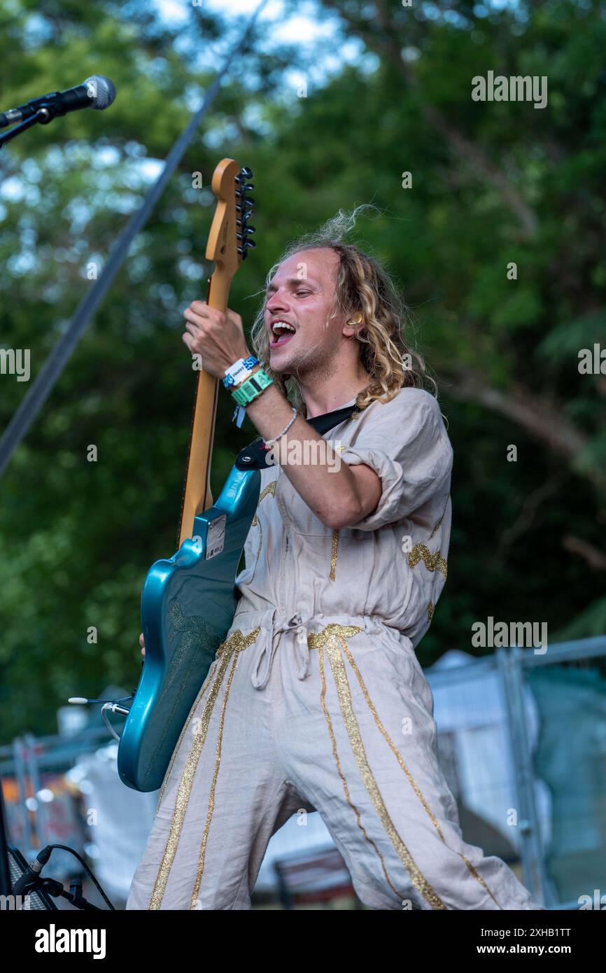 L'uomo dai capelli lunghi e biondi suona una chitarra Fender Jaguar blu: Catturare l'energia del Funk e della musica rock. Foto Stock