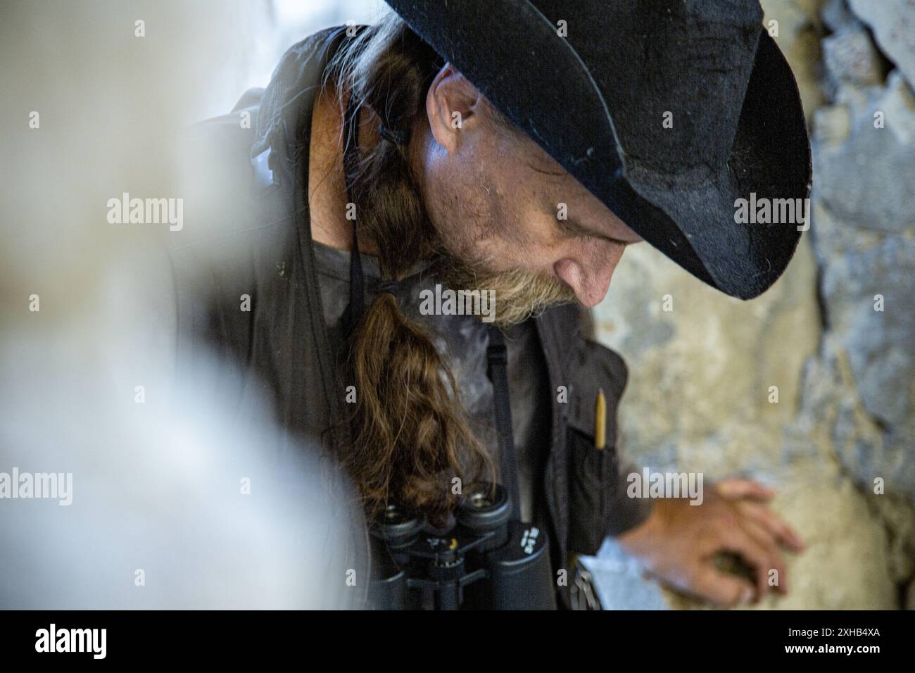 Emotional Ritratto di un uomo in abiti da viaggio e cappello che si arrampicano sullo sfondo di un muro di una fortezza. Archeologia. Studio. Viaggio. Foto Stock