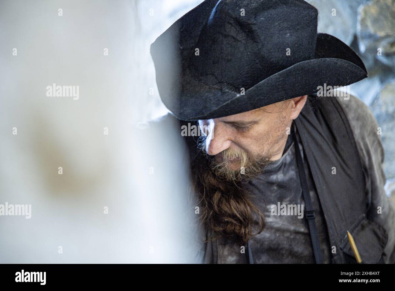 Emotional Ritratto di un uomo in abiti da viaggio e cappello che si arrampicano sullo sfondo di un muro di una fortezza. Archeologia. Studio. Viaggio. Vista laterale. Foto Stock