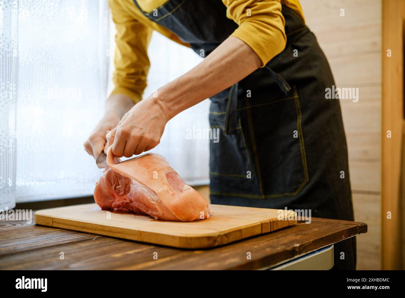 L'uomo irriconoscibile in grembiule taglia la pelle dalla spalla di maiale cruda Foto Stock