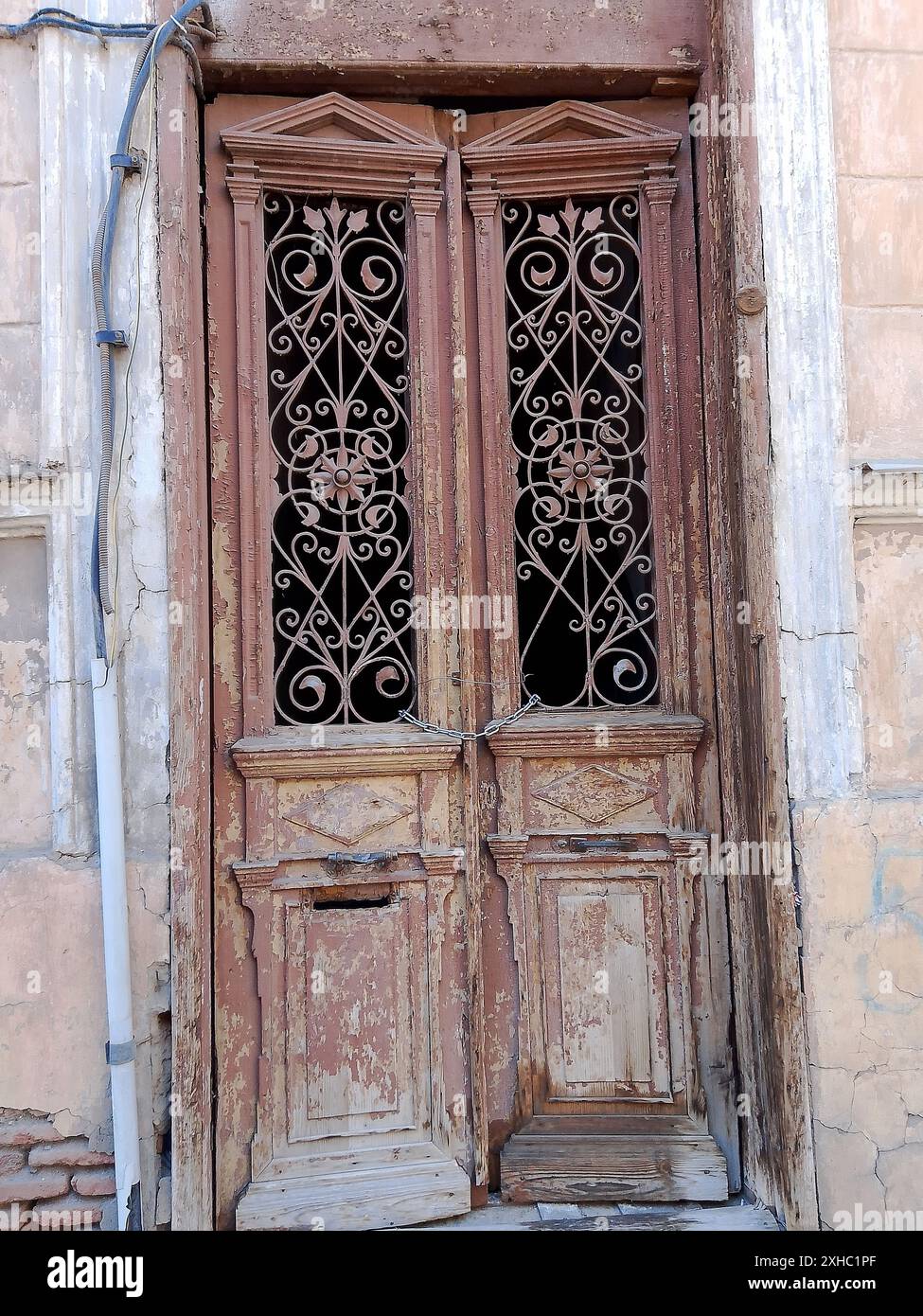 Questa immagine cattura il fascino rustico di una coppia di porte in legno intemperie, ognuna decorata con intricati lavori in ferro e motivi. Le porte sono una prova Foto Stock