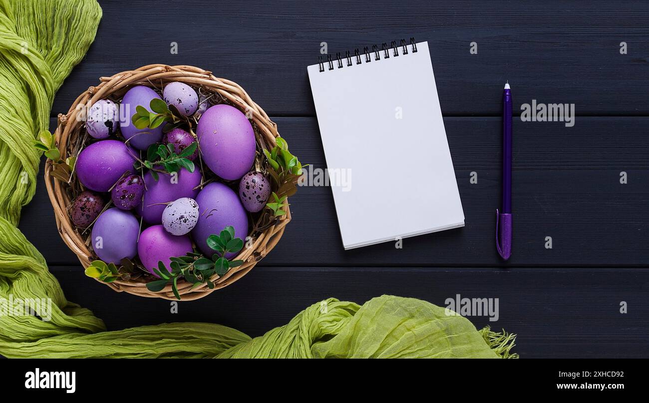 Uova di Pasqua, viola e lilla, con un blocco note per scrivere, fare un mockup, su un tavolo di legno grigio, cartolina pasquale, striscione, messa a fuoco selettiva, orizzontale Foto Stock
