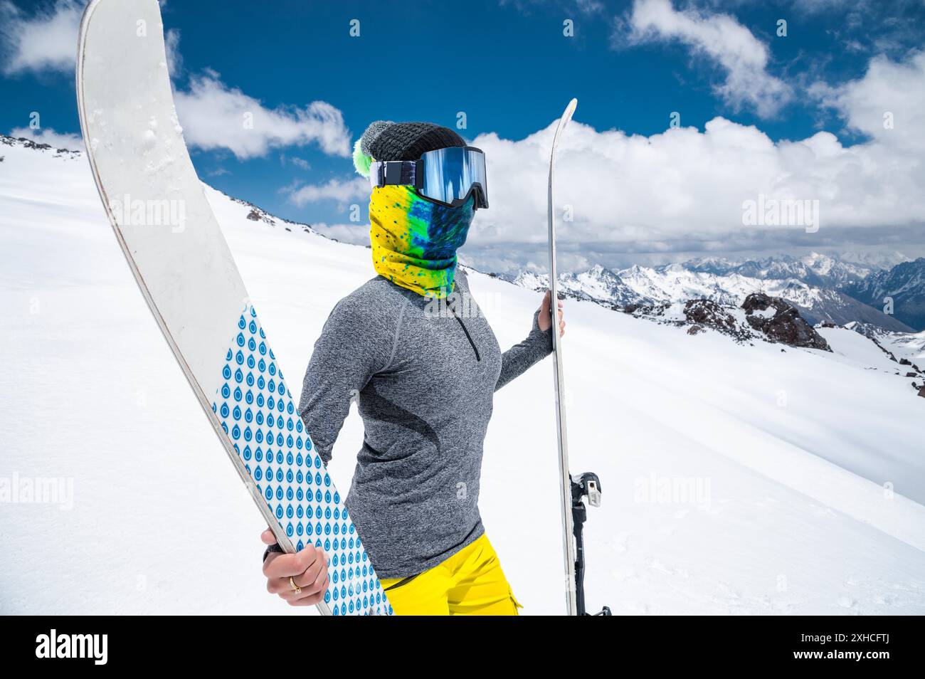 Ritratto di una ragazza snella in un buff e una balaclava in una maschera da sci e un cappello con una faccia chiusa accanto agli sci sullo sfondo di neve Foto Stock