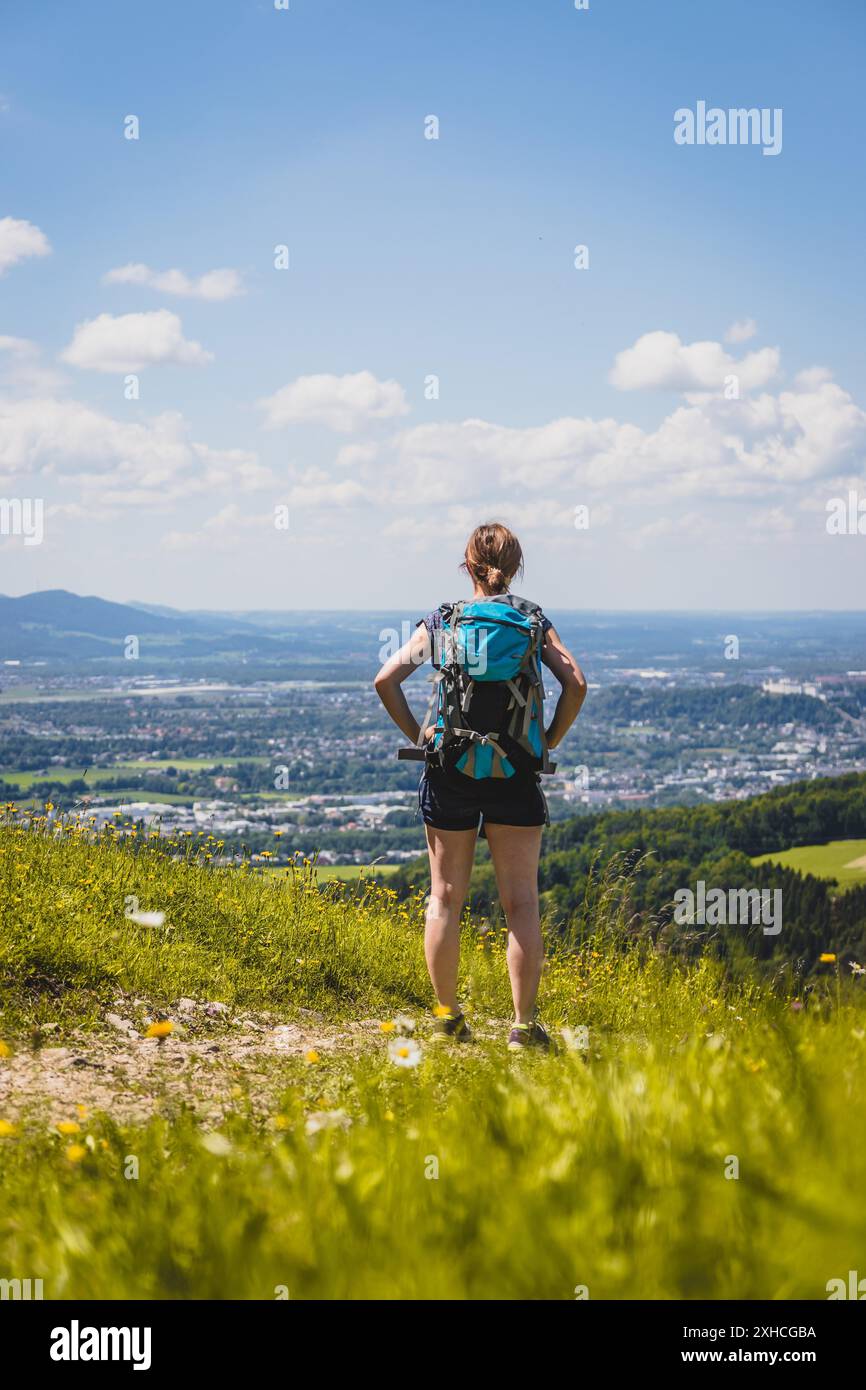 Ragazza sportiva in un viaggio a piedi è in piedi sul prato e godere della vista sulla città lontano Foto Stock