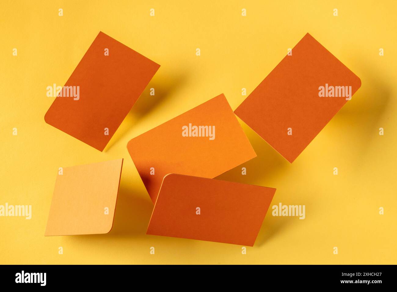 Biglietti da visita arancioni spessi con un angolo arrotondato, fluttuante su uno sfondo di carta giallo, un mockup per una presentazione di design creativo Foto Stock