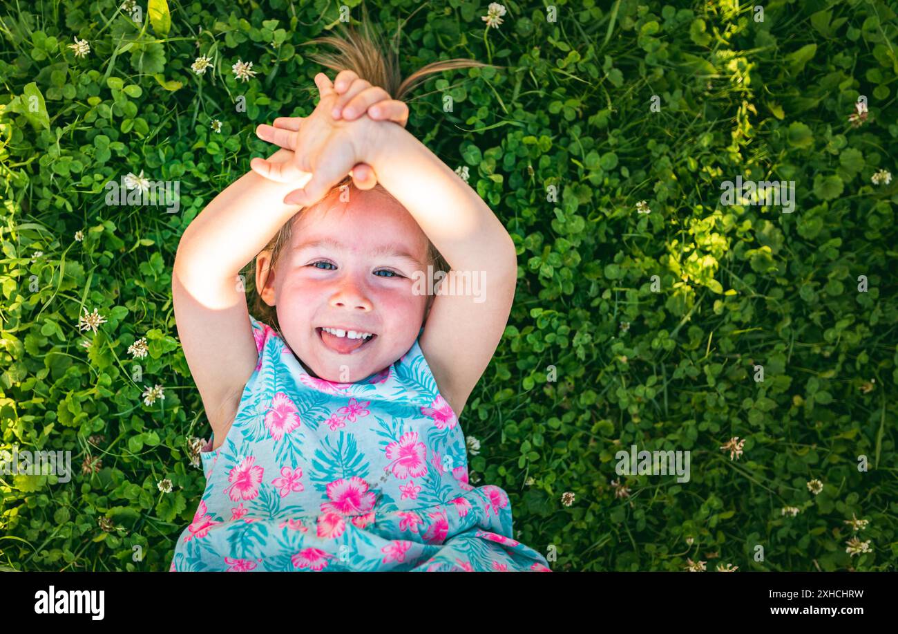 Bella bambina sdraiata su erba ridendo e guardando in su. bambino di 2-3 anni in natura nella soleggiata giornata estiva Foto Stock