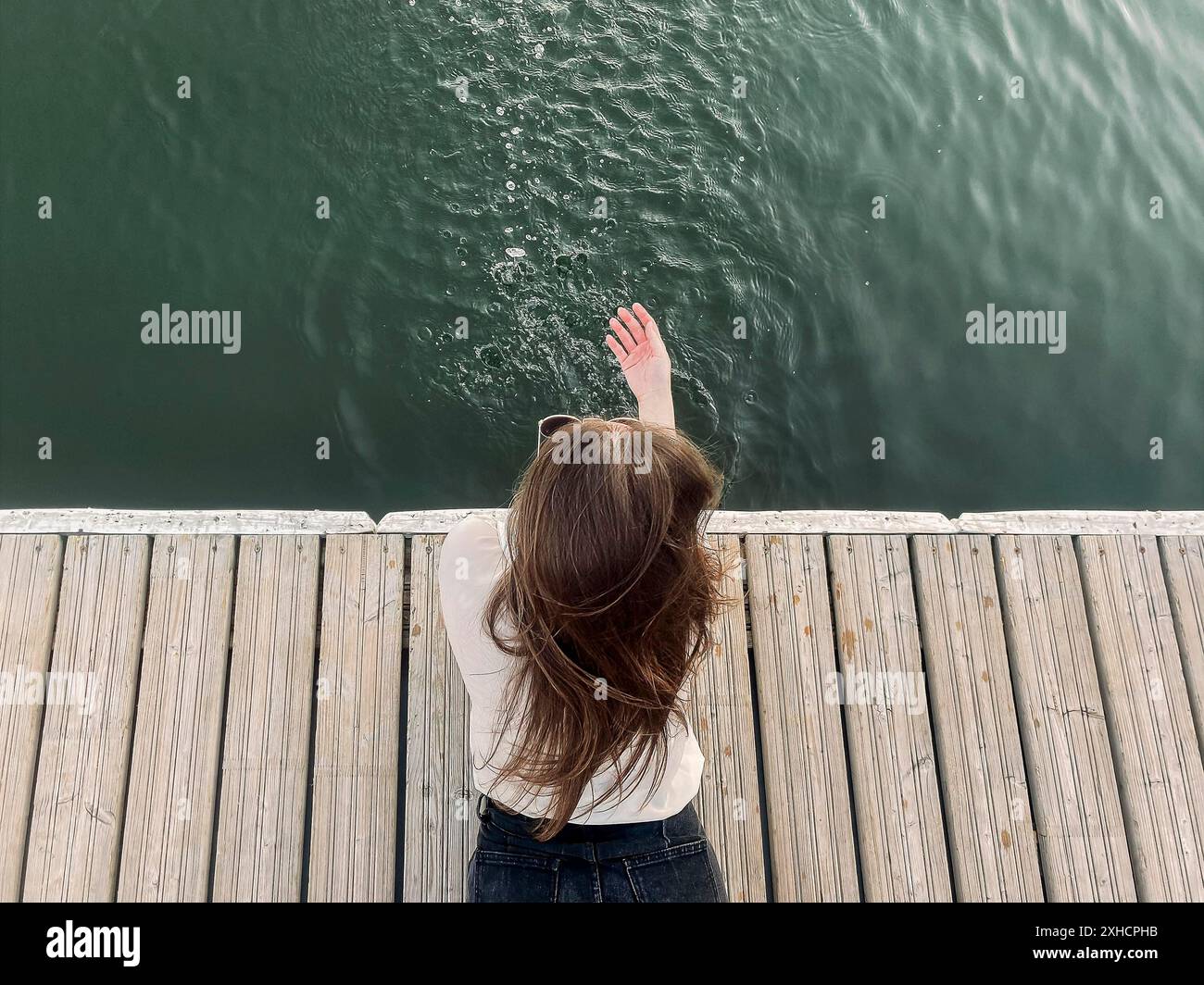 Giovane femmina di brunette sdraiata sulla banchina e spruzzi d'acqua pulita del lago il giorno d'estate Foto Stock